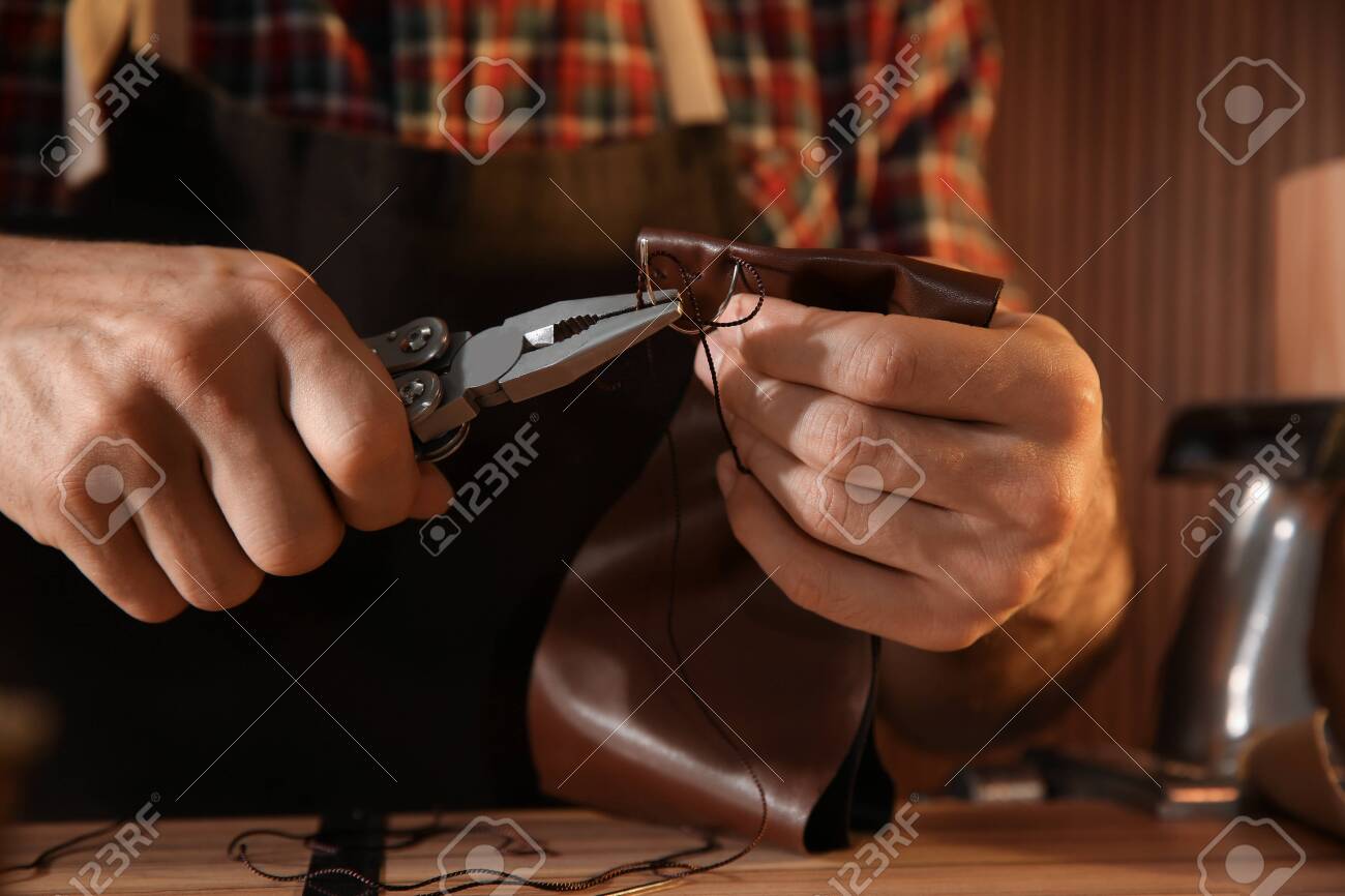 Man sewing piece of leather at table, closeup - 141145376 Man sewing piece of leather at table, closeup - 141145376