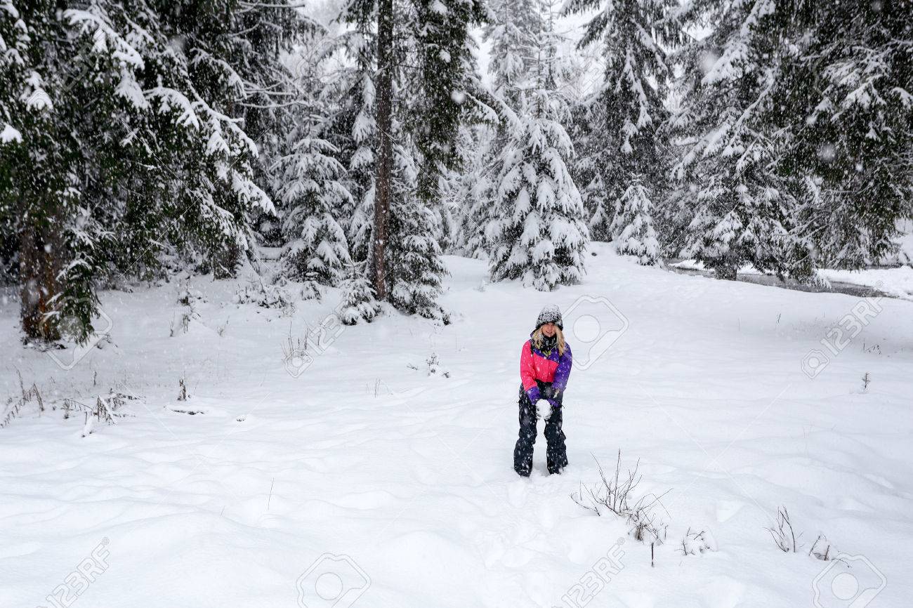 かわいいブロンドの女の子のプレイは 冬の雪に覆われた森雪玉します ピンク色スキー スーツと黒の帽子の女の子 たくさんの雪の中で木の背景 の写真素材 画像素材 Image