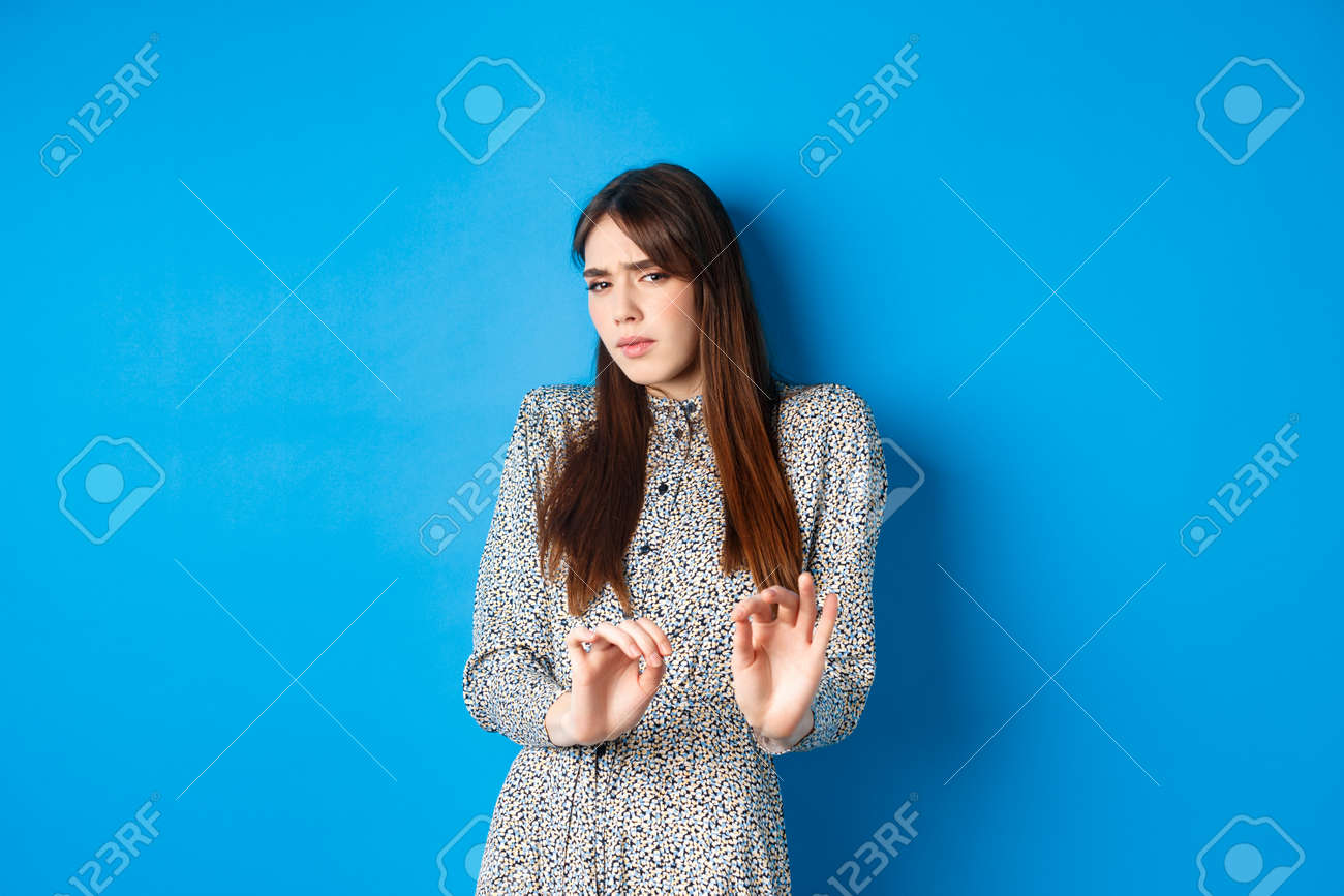 いやがる女 ここから遠ざけるように頼むうんざりして嫌がる女性、ブロックジェスチャーを示し、手を上げてあなたを止め、青い背景の上に立っているの写真素材・画像素材  Image 163453344