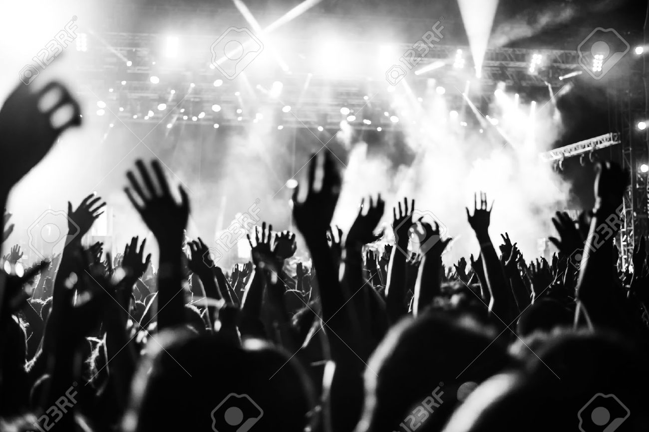 Black and white photo of audience with hands raised at a music festival and lights streaming