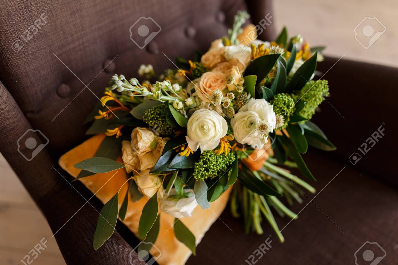 ブライダル ブーケ 花嫁のブーケ 白牡丹 クリーム色のバラとオレンジ色の絹のリボンで飾られた緑の美しい花束に茶色の椅子にオレンジ色のクッションの背景にあります の写真素材 画像素材 Image