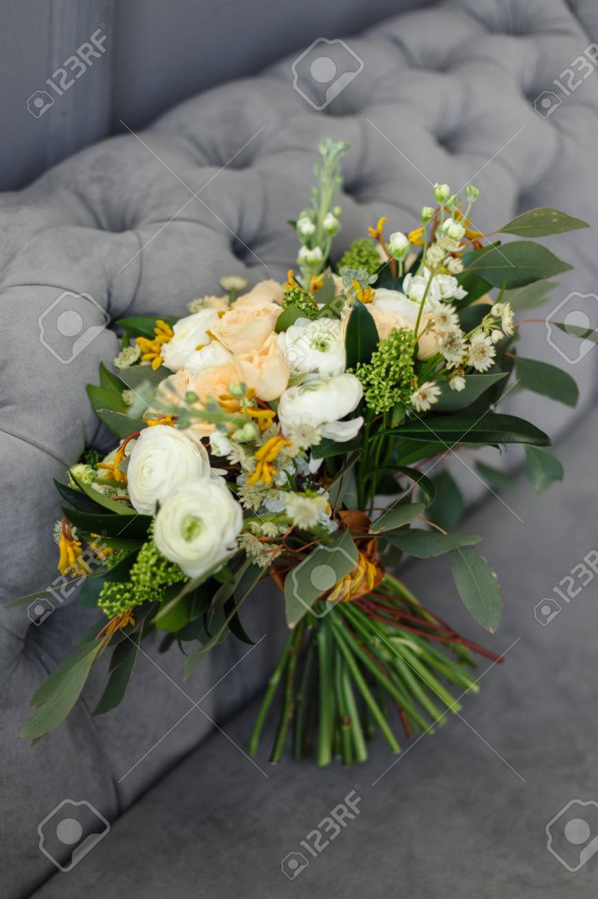 ブライダル ブーケ 花嫁のブーケ 白牡丹 クリーム色のバラとオレンジ色の絹のリボンで飾られた緑の美しい花束がグレーのソファの上にあります の写真素材 画像素材 Image