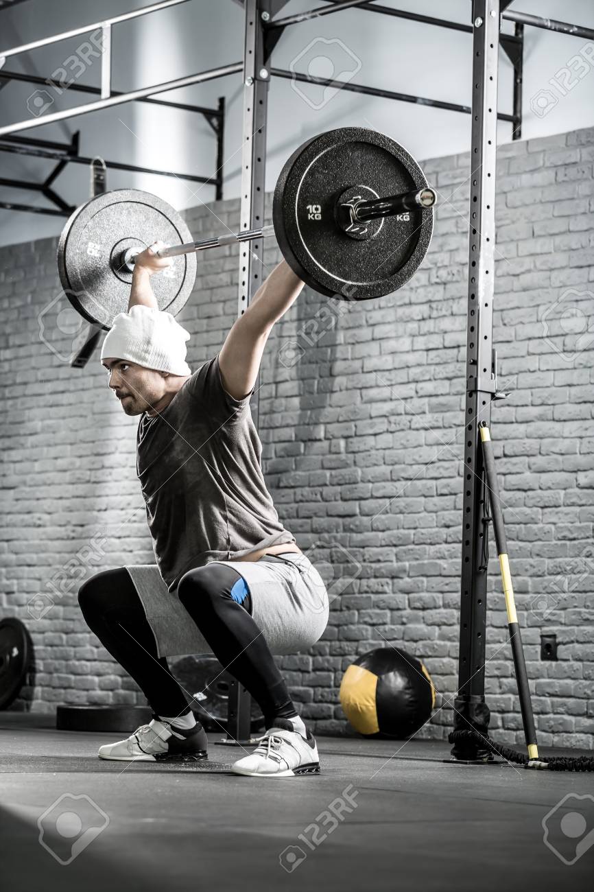Magnifique Homme Avec Une Barbe Souleve Une Barre Au Dessus De Sa Tete Dans Le Squat Dans Le Gymnase Sur Le Gris Mur De Briques De Fond Il Porte Des Vetements De Sport