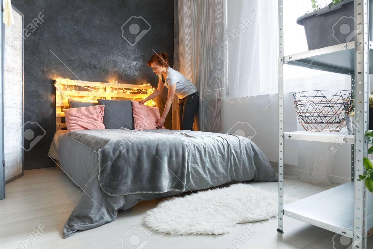 Junge Frau macht ein Bett in ihrem kleinen gemütlichen Schlafzimmer Junge Frau macht ein Bett in ihrem kleinen gemütlichen Schlafzimmer