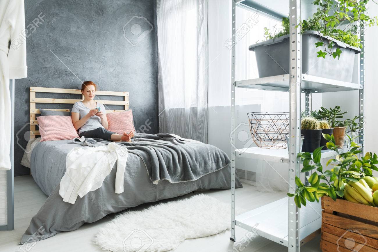Young Woman Sitting On Bed In Cozy Bedroom With Simple Decor