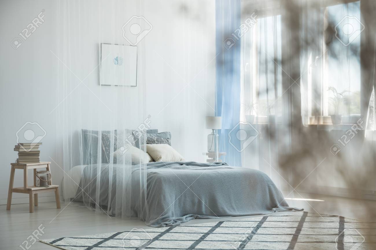 カーペット グレー寝室のインテリアのベールの下のキングサイズのベッドの横に木製のスツールの本 の写真素材 画像素材 Image