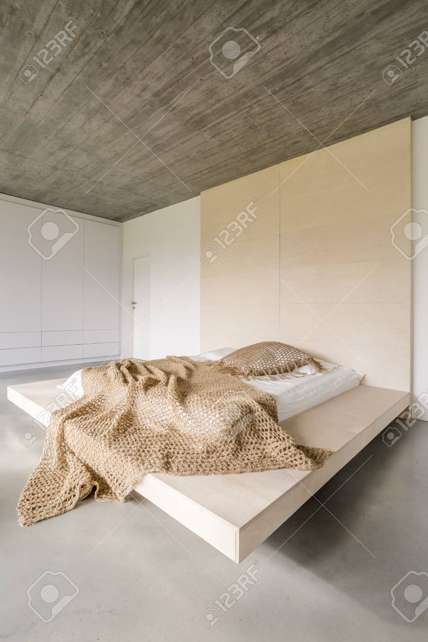 Modern Bed On Wooden Platform In Bright Room With Concrete Ceiling