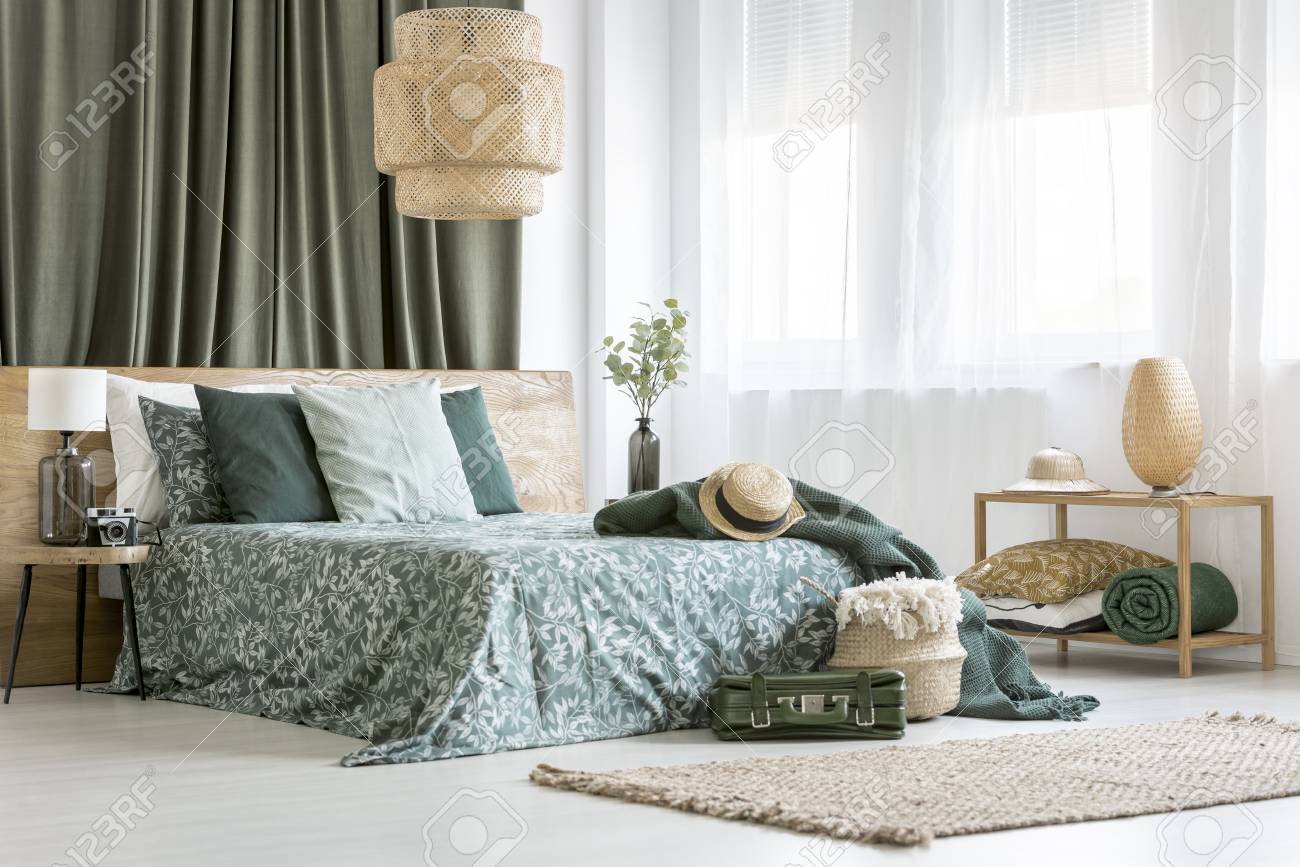 rattan lampe über kingsize-bett mit floralen gänseblümchen im hellen  schlafzimmer mit lampe und koffer
