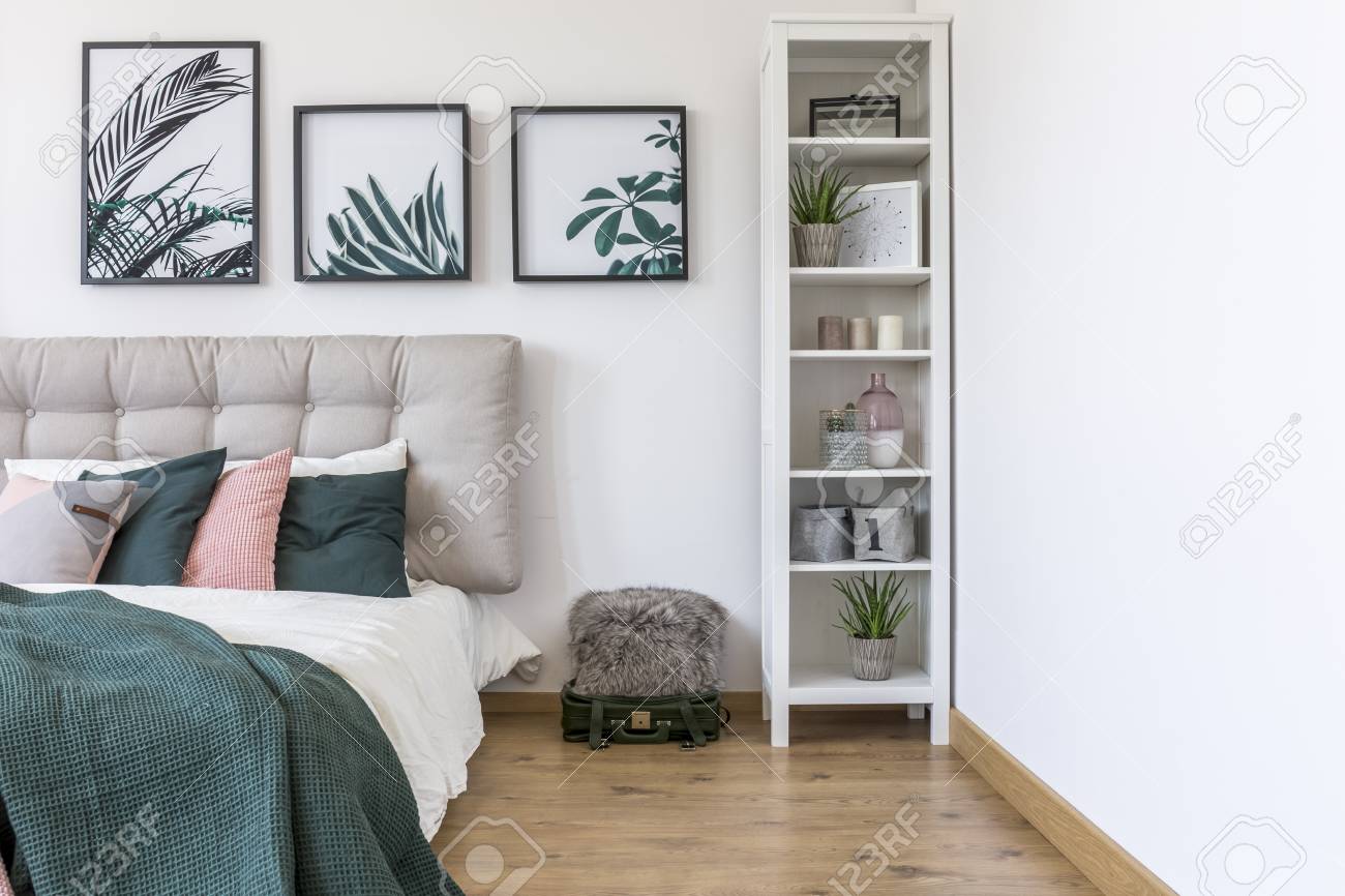 Weißer Schrank neben Bett mit grünen Kissen gegen die Wand der Galerie mit Plakaten im Schlafzimmer Interieur Weißer Schrank neben Bett mit grünen Kissen gegen die Wand der Galerie mit Plakaten im Schlafzimmer Interieur