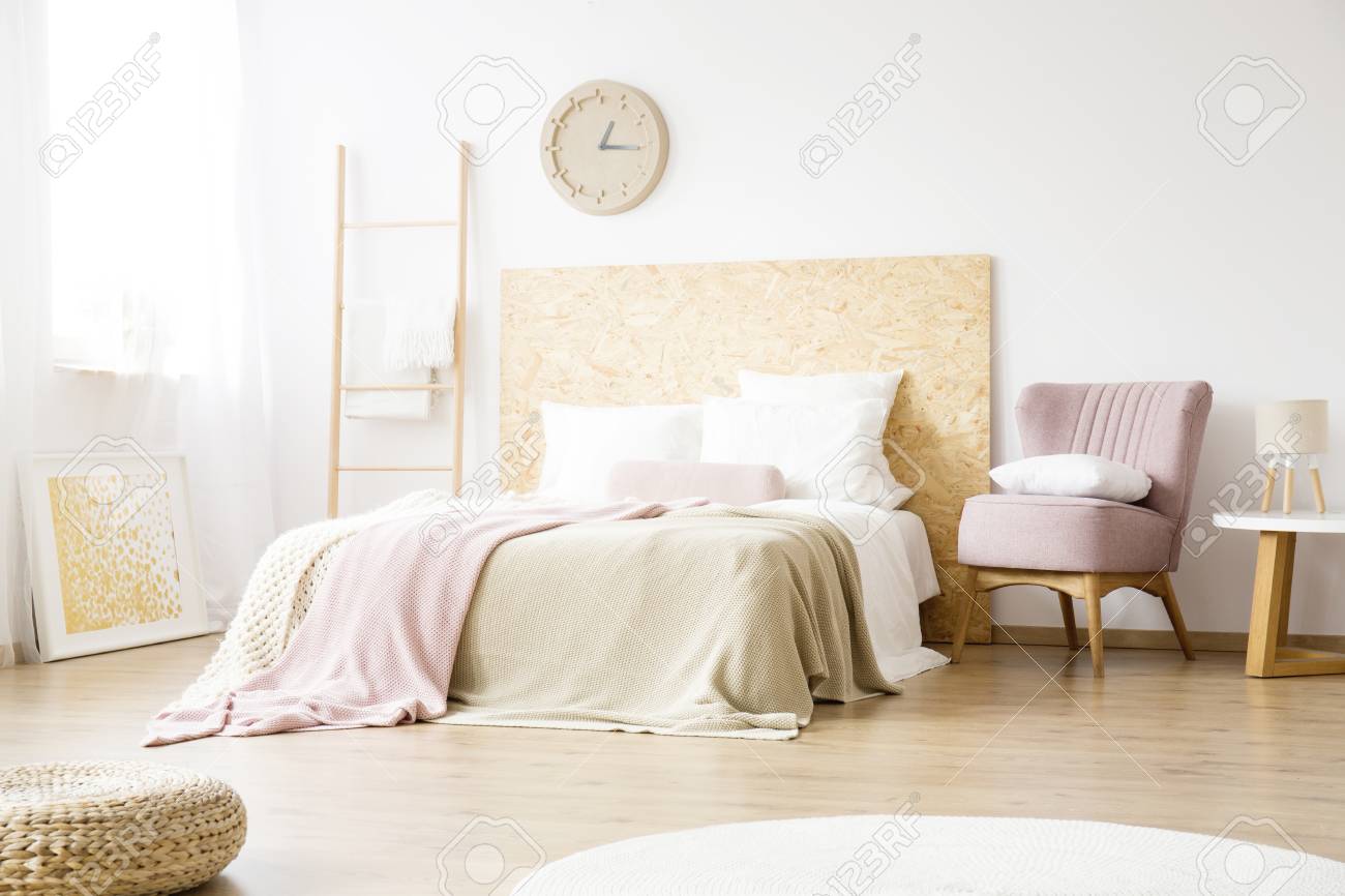 シンプルなベッドルームにピンクとベージュの毛布が付いているベッドの隣に立つピンクのアームチェア の写真素材 画像素材 Image