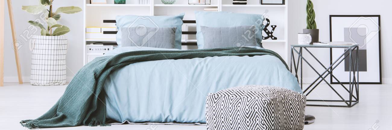 Bed With Pastel Blue Bedclothes And Green Blanket Standing In