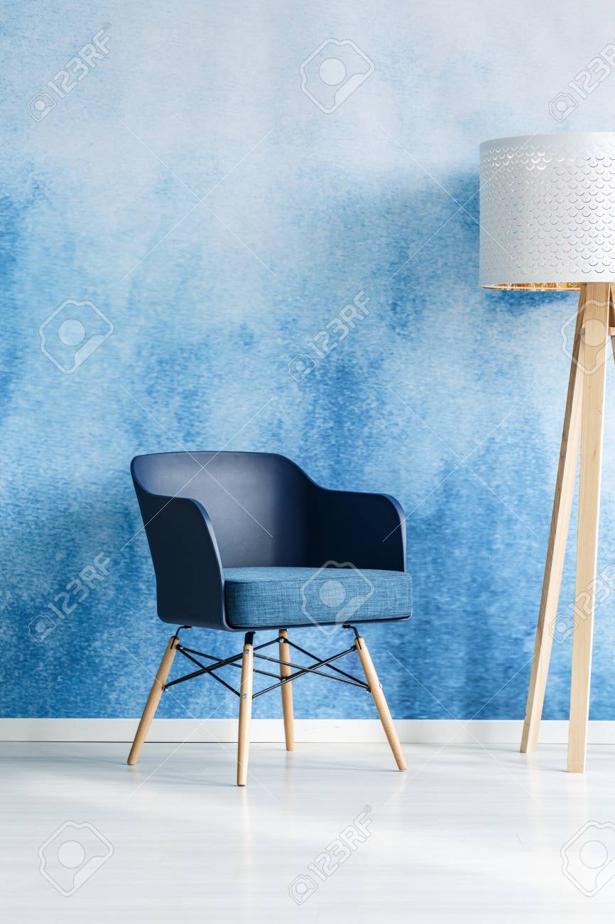 Navy blue armchair next to white wooden lamp in modern living room interior with ombre wall