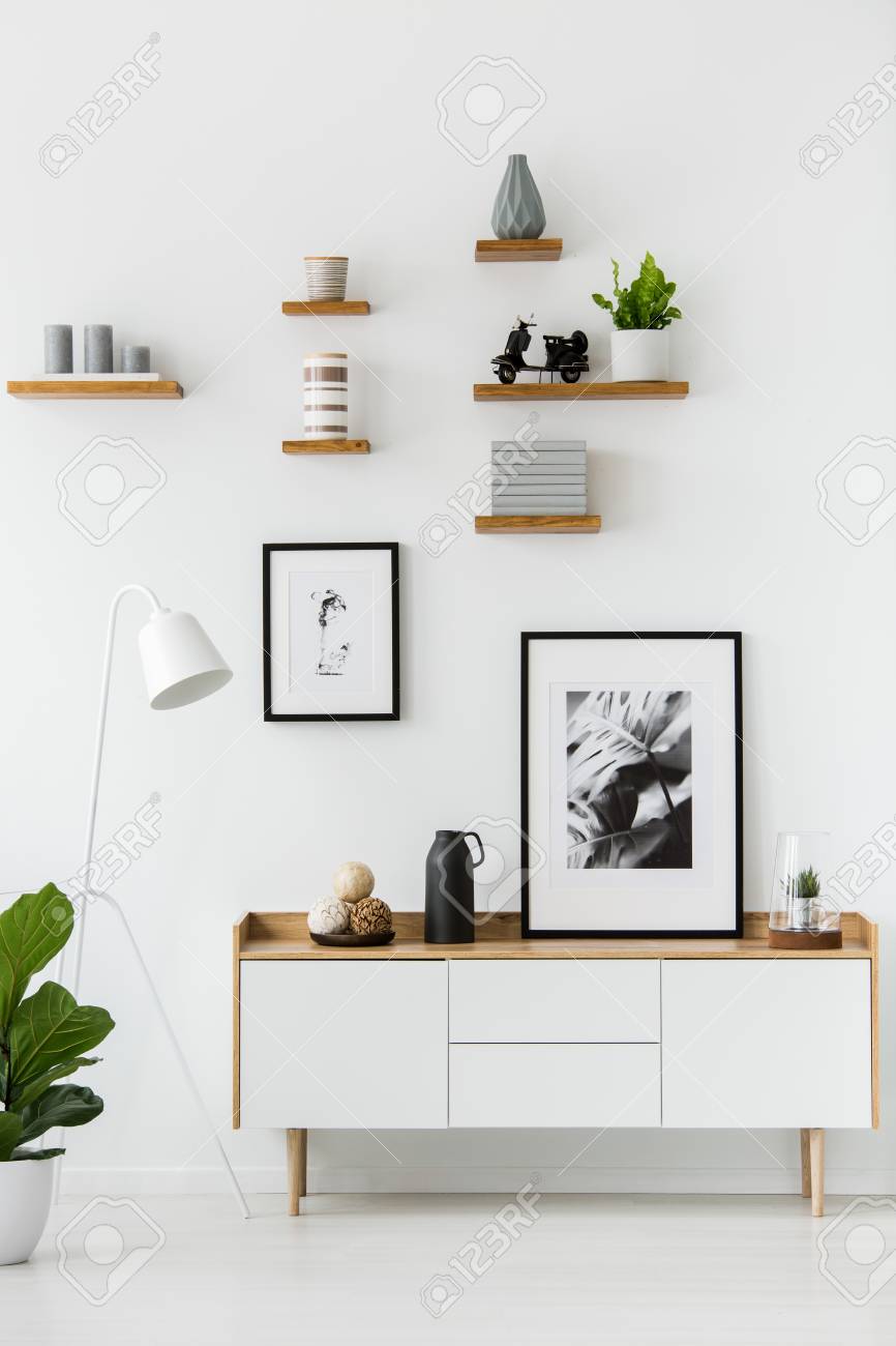 Poster on wooden cupboard in white living room interior with lamp and plant. Real photo - 101667628 Poster on wooden cupboard in white living room interior with lamp and plant. Real photo - 101667628