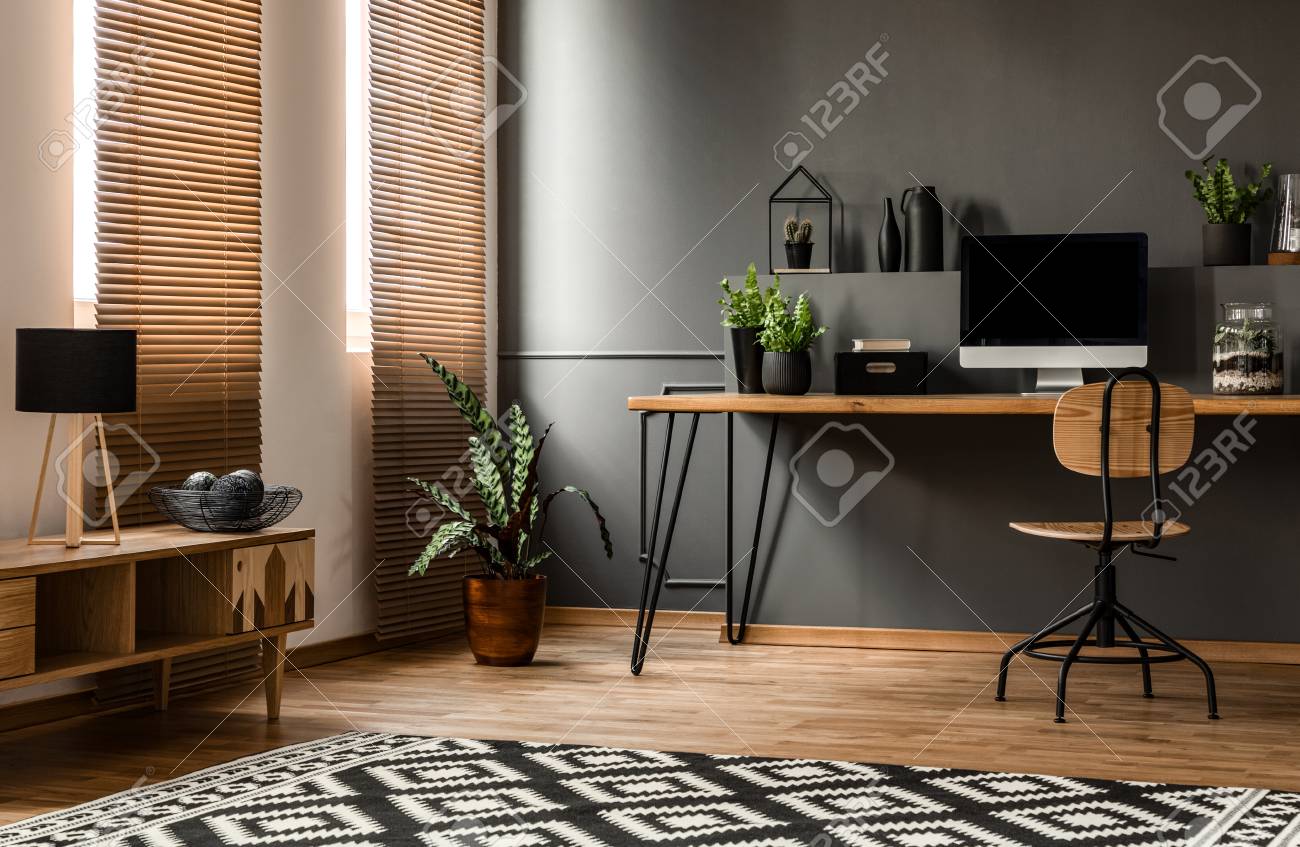 Lamp on wooden cupboard near plant and desk with computer monitor in dark grey workspace interior - 107030617 Lamp on wooden cupboard near plant and desk with computer monitor in dark grey workspace interior - 107030617