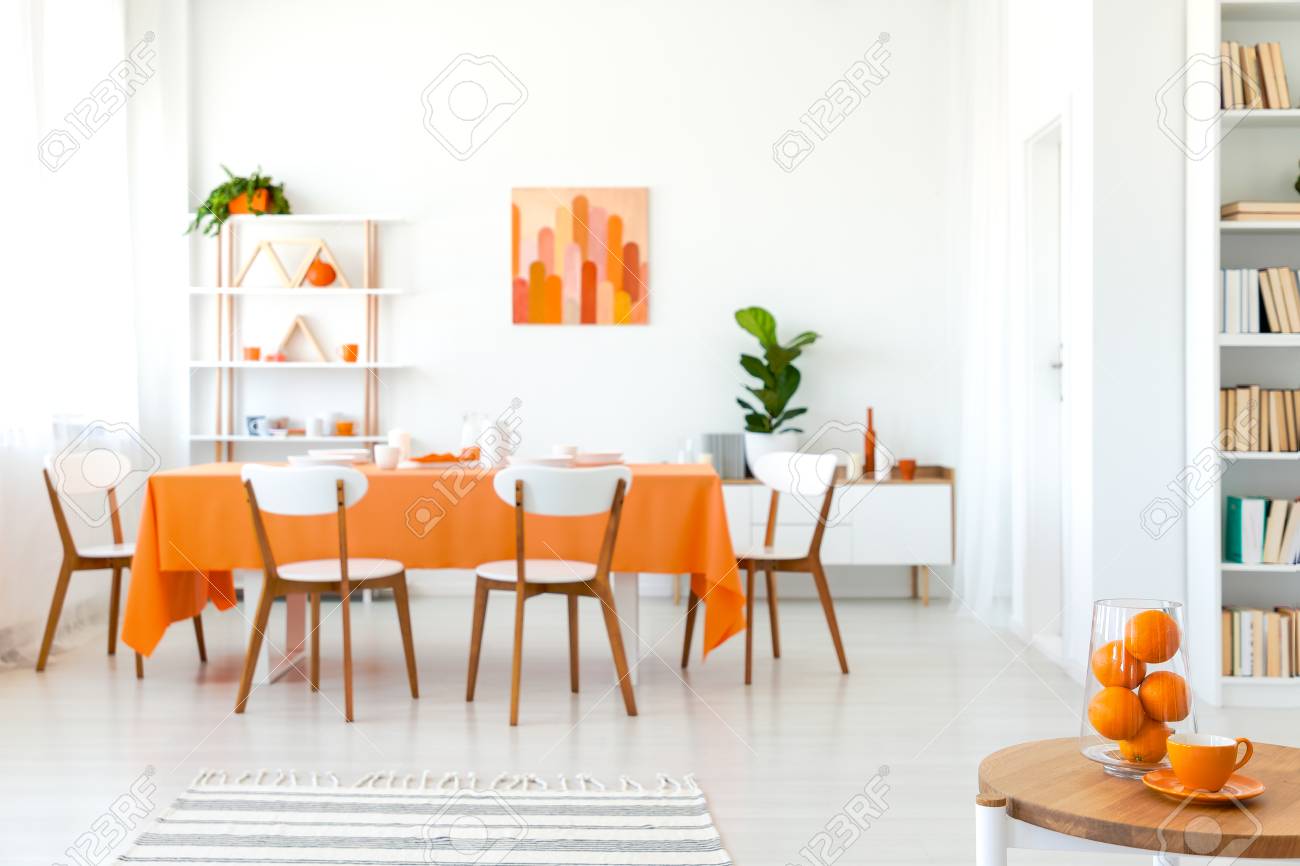 White Chairs At Table With Orange Cloth In Modern Dining Room Stock Photo