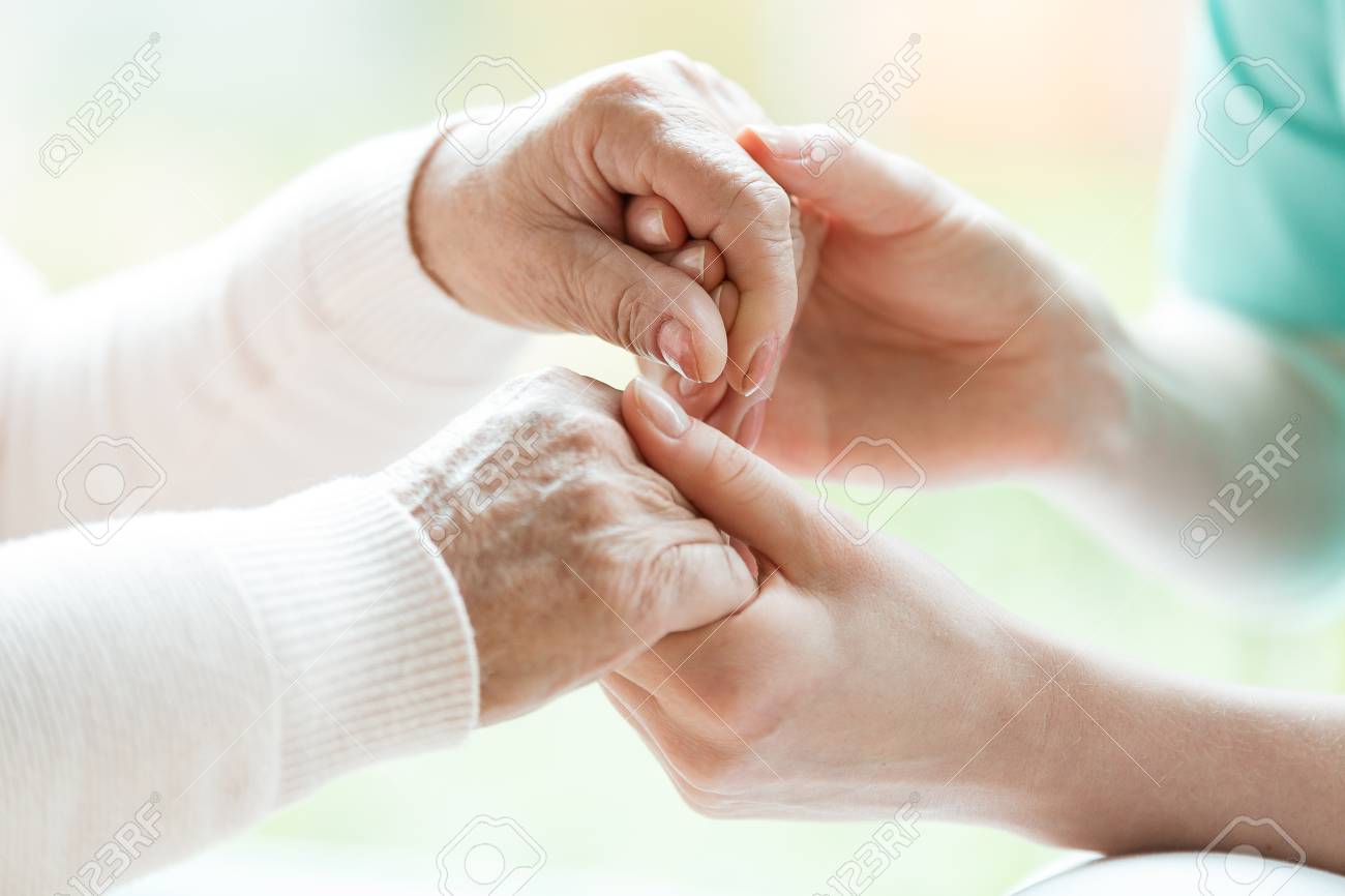 Closeup of the hands of a young woman holding hands of an elderly lady - 113820651 Closeup of the hands of a young woman holding hands of an elderly lady - 113820651