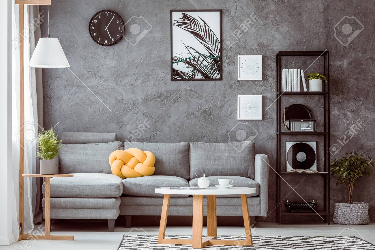 Grey concrete wall in modern living room with industrial black metal bookshelf next to comfortable sofa with yellow knot pillow - 113820659 Grey concrete wall in modern living room with industrial black metal bookshelf next to comfortable sofa with yellow knot pillow - 113820659