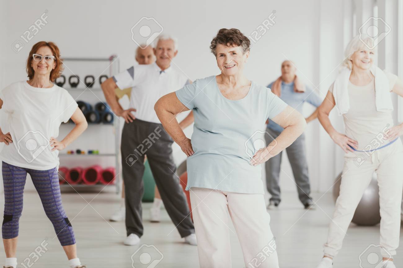 Happy senior woman holding hips during gymnastic classes for elderly people - 113820913 Happy senior woman holding hips during gymnastic classes for elderly people - 113820913