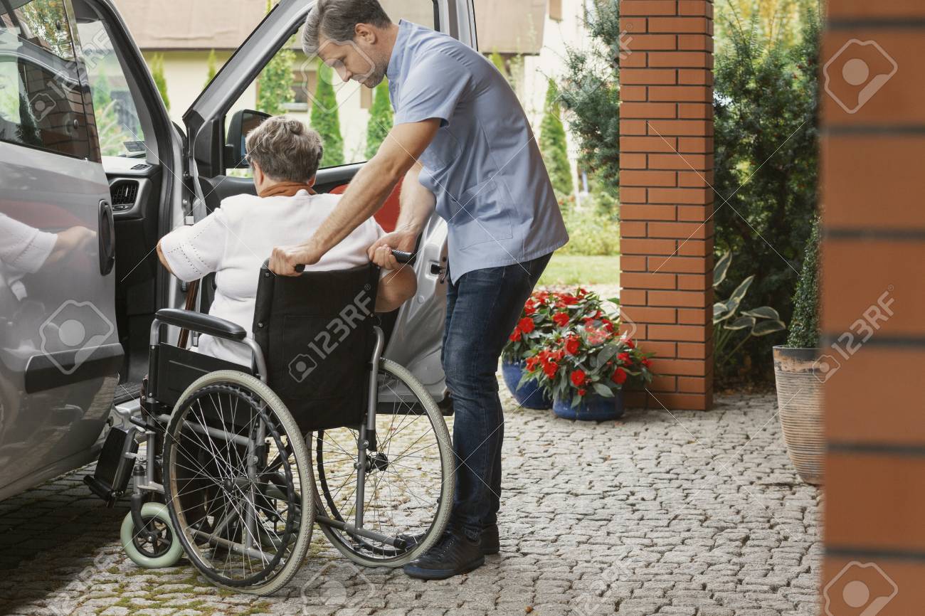 Helpful male nurse with senior lady on wheelchair helping her get in to the car - 114496875 Helpful male nurse with senior lady on wheelchair helping her get in to the car - 114496875