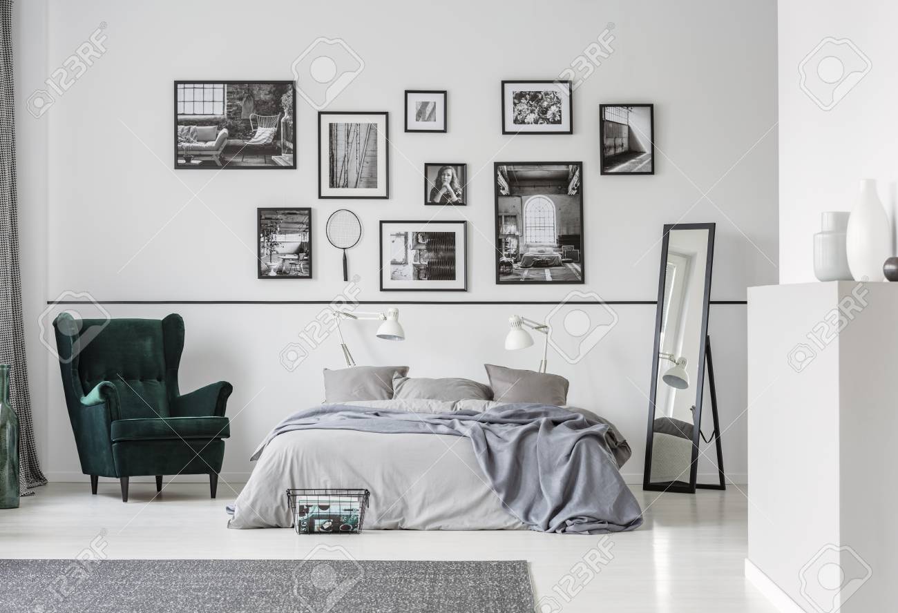 Grey bed between armchair and mirror in bedroom interior with gallery and lamps. Real photo - 115417295 Grey bed between armchair and mirror in bedroom interior with gallery and lamps. Real photo - 115417295