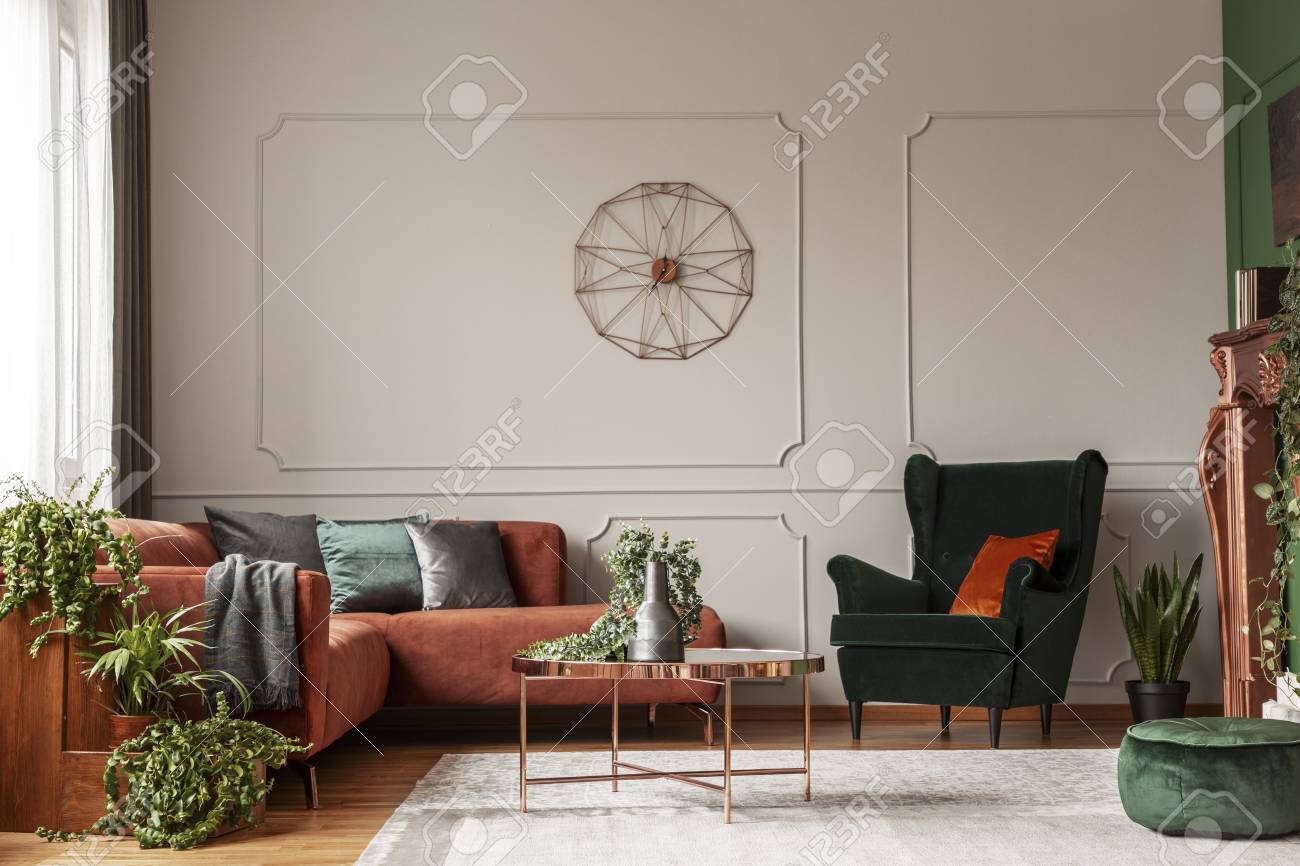 Velvet emerald green armchair with orange pillow next to corner sofa and coffee table - 119584490 Velvet emerald green armchair with orange pillow next to corner sofa and coffee table - 119584490