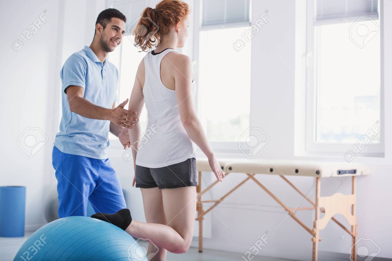 Physiotherapist supporting woman during rehabilitation with ball - 123454135 Physiotherapist supporting woman during rehabilitation with ball - 123454135