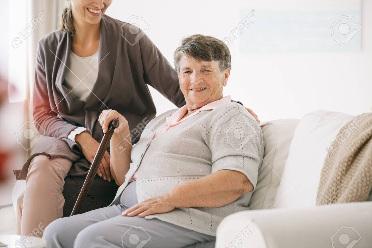 Older disabled woman with a stick in nursing home with caretaker - 128921553 Older disabled woman with a stick in nursing home with caretaker - 128921553