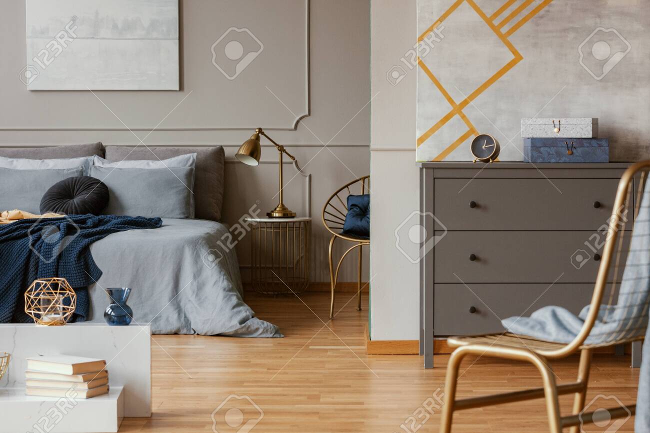Trendy Bedroom Interior With Grey Commode And Golden Chair