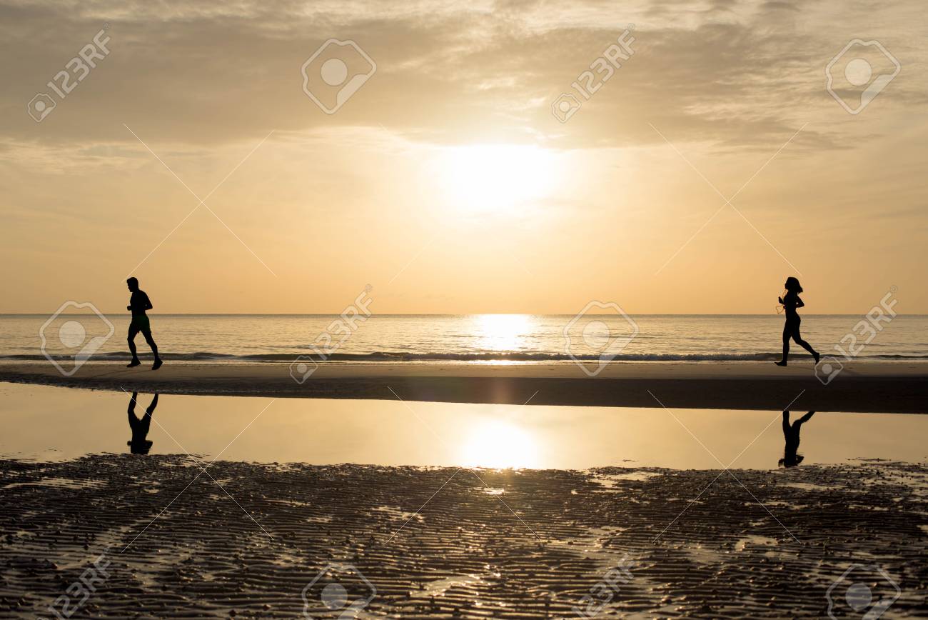 man and woman running together on the beach in sunset sunrise