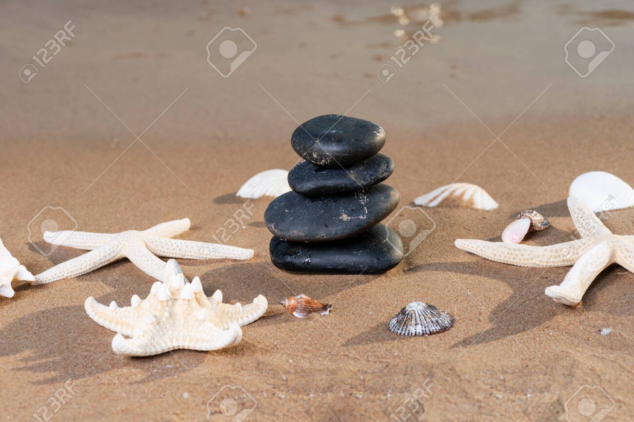 Spa composition - stacked Basalt Stones, Seashells and Sea Stars on the beach at sunrise in front of the ocean. Wellness, Balance and Relax concept. - 128873561 Spa composition - stacked Basalt Stones, Seashells and Sea Stars on the beach at sunrise in front of the ocean. Wellness, Balance and Relax concept. - 128873561