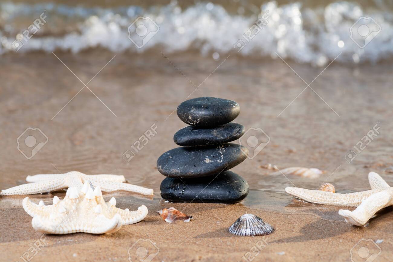 Spa composition - stacked Basalt Stones, Seashells and Sea Stars on the beach at sunrise in front of the ocean. Wellness, Balance and Relax concept. - 128873569 Spa composition - stacked Basalt Stones, Seashells and Sea Stars on the beach at sunrise in front of the ocean. Wellness, Balance and Relax concept. - 128873569