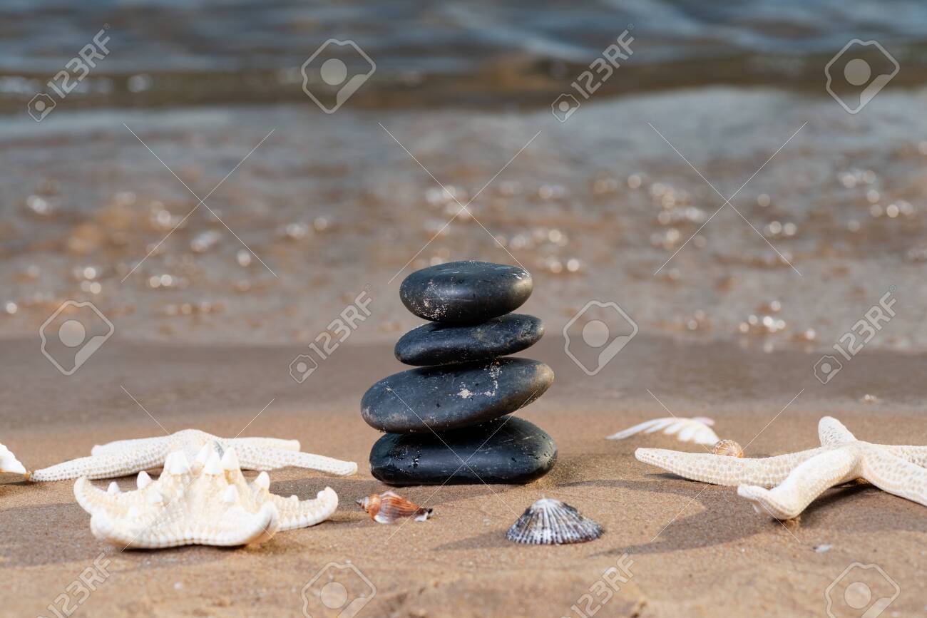 Spa composition - stacked Basalt Stones, Seashells and Sea Stars on the beach at sunrise in front of the ocean. Wellness, Balance and Relax concept. - 128873574 Spa composition - stacked Basalt Stones, Seashells and Sea Stars on the beach at sunrise in front of the ocean. Wellness, Balance and Relax concept. - 128873574