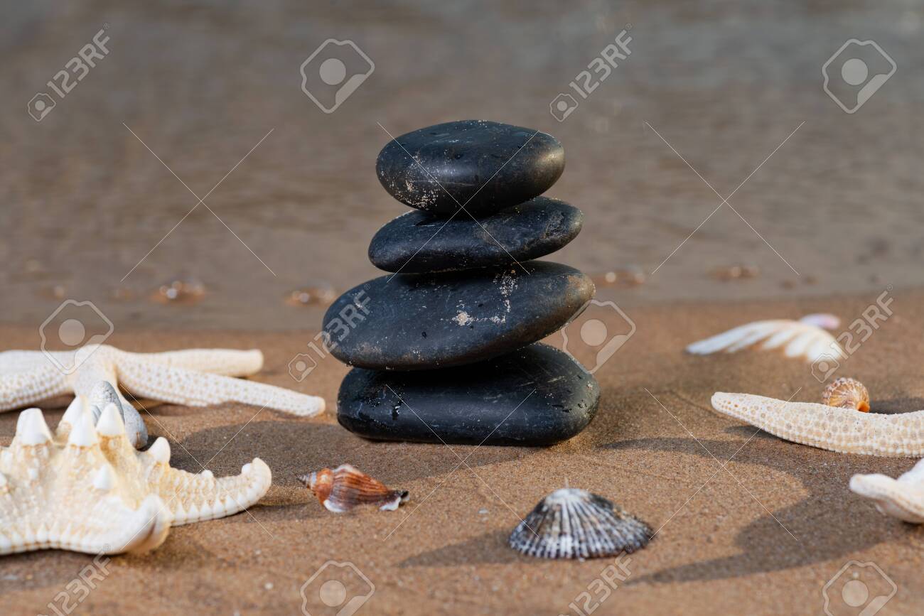 Spa composition - stacked Basalt Stones, Seashells and Sea Stars on the beach at sunrise in front of the ocean. Wellness, Balance and Relax concept. - 128873516 Spa composition - stacked Basalt Stones, Seashells and Sea Stars on the beach at sunrise in front of the ocean. Wellness, Balance and Relax concept. - 128873516