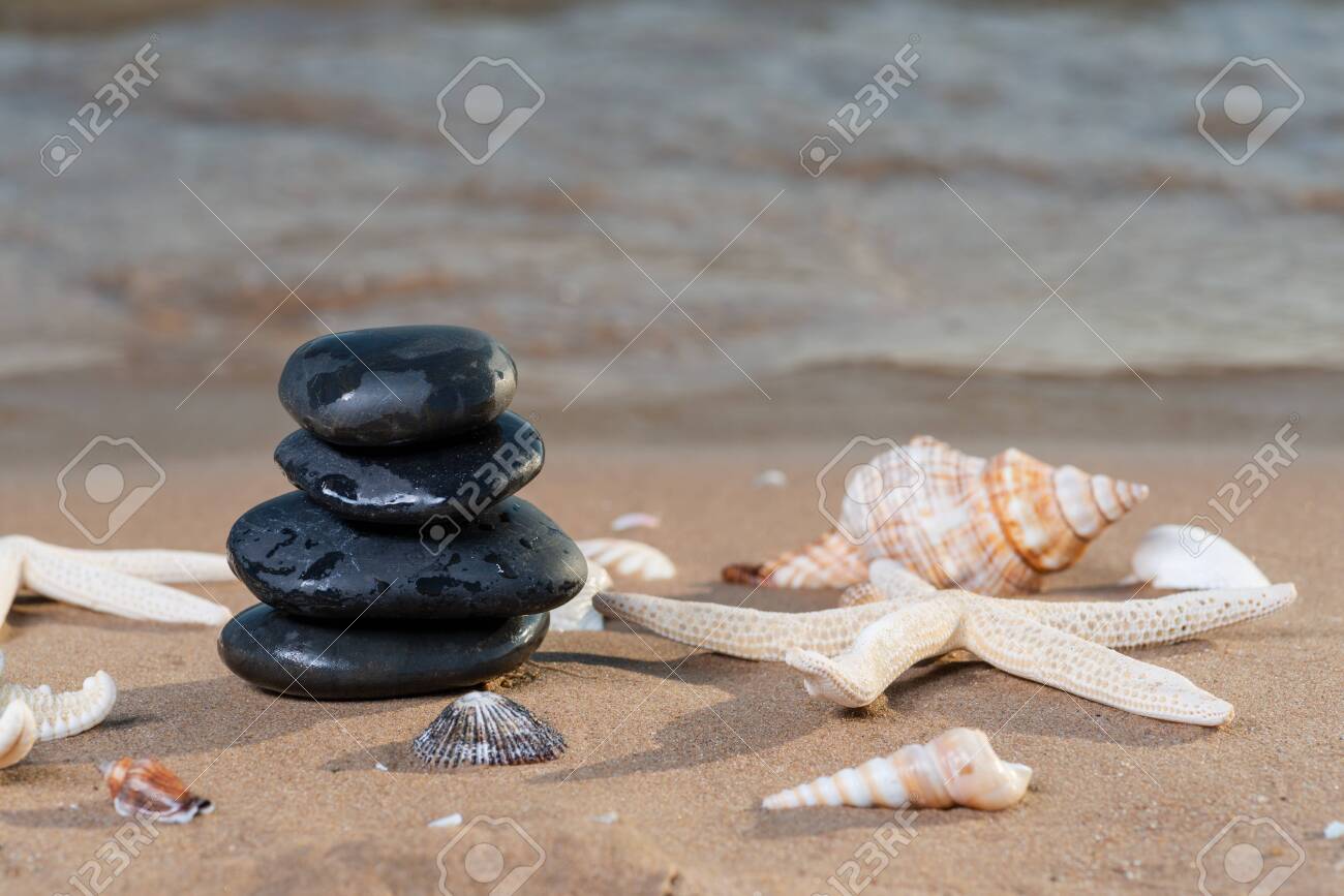 Spa composition - stacked Basalt Stones, Seashells and Sea Stars on the beach at sunrise in front of the ocean. Wellness, Balance and Relax concept. - 128873524 Spa composition - stacked Basalt Stones, Seashells and Sea Stars on the beach at sunrise in front of the ocean. Wellness, Balance and Relax concept. - 128873524