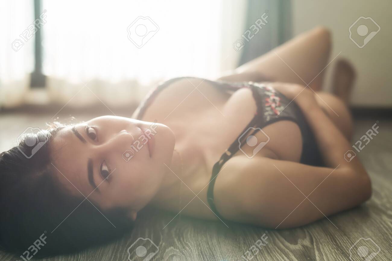 Beautiful Tan Asian Woman With Sexy Black Bra Lying On Wooden Flloor Near Windows With Flare Natural Light. Portrait Of Brunette Girl With Natural Big Boobs