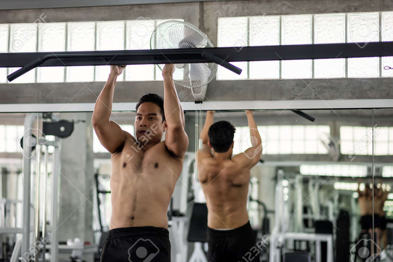 Muscular Strong Asian Man With Topless Nude Torso Exercise By Pulling Up On  Horizontal Bar With Body Reflection On Mirror At Sport Fitness Gym.  Bodybuilding And Healthy Lifestyle Concept. Stock Photo, Picture
