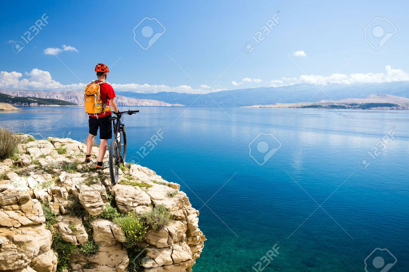 Mountain biking rider with bike looking at inspiring sea and mountains landscape. Man cycling MTB on enduro rocky trail path at sea side. Summer sport, training fitness motivation and inspiration. - 58181582 Mountain biking rider with bike looking at inspiring sea and mountains landscape. Man cycling MTB on enduro rocky trail path at sea side. Summer sport, training fitness motivation and inspiration. - 58181582