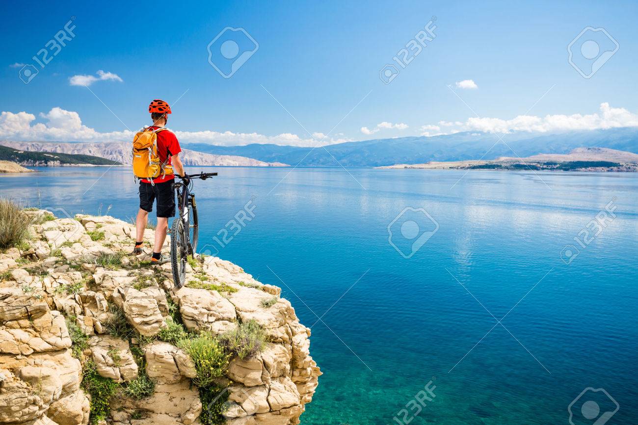 Mountain biker looking at view and traveling on bike in summer sea landscape. Man rider cycling MTB on country road or single track. Fitness motivation, inspiration in beautiful inspirational view. - 58584076 Mountain biker looking at view and traveling on bike in summer sea landscape. Man rider cycling MTB on country road or single track. Fitness motivation, inspiration in beautiful inspirational view. - 58584076