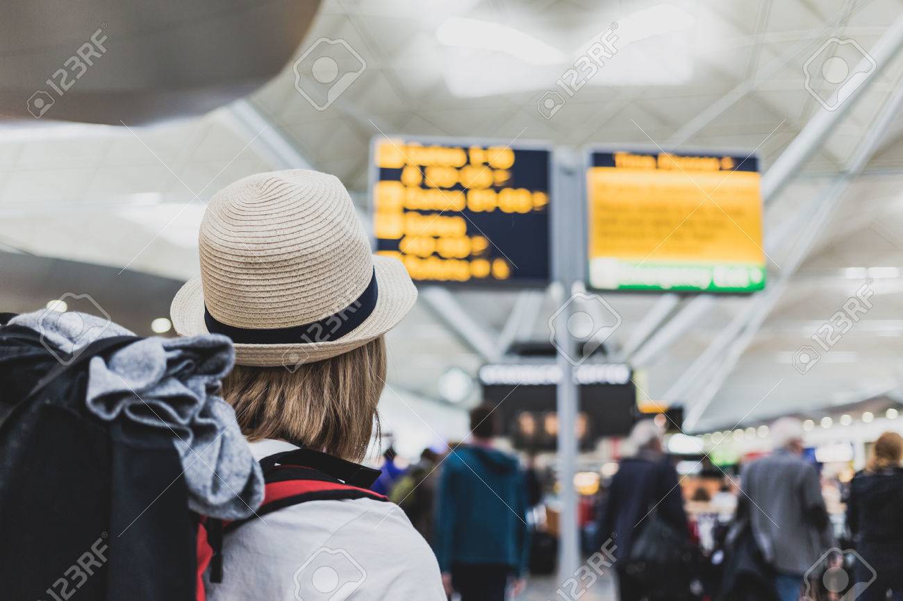 Woman hiker with backpack in airport looking at the flight information checking an international flight to travel destination. - 65114186 Woman hiker with backpack in airport looking at the flight information checking an international flight to travel destination. - 65114186