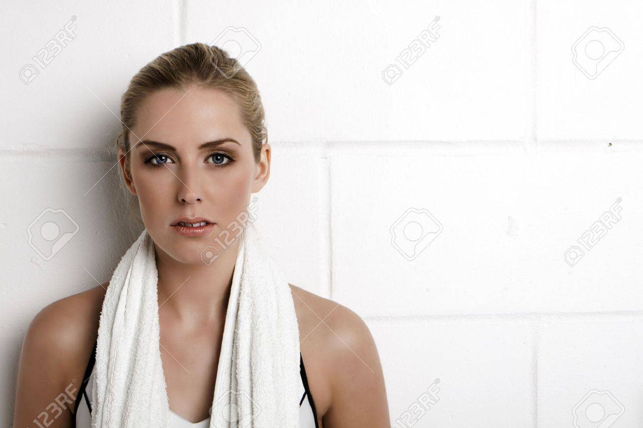 Beautiful blond woman standing against a wall in a gym with a towel around her neck. - 11287257 Beautiful blond woman standing against a wall in a gym with a towel around her neck. - 11287257