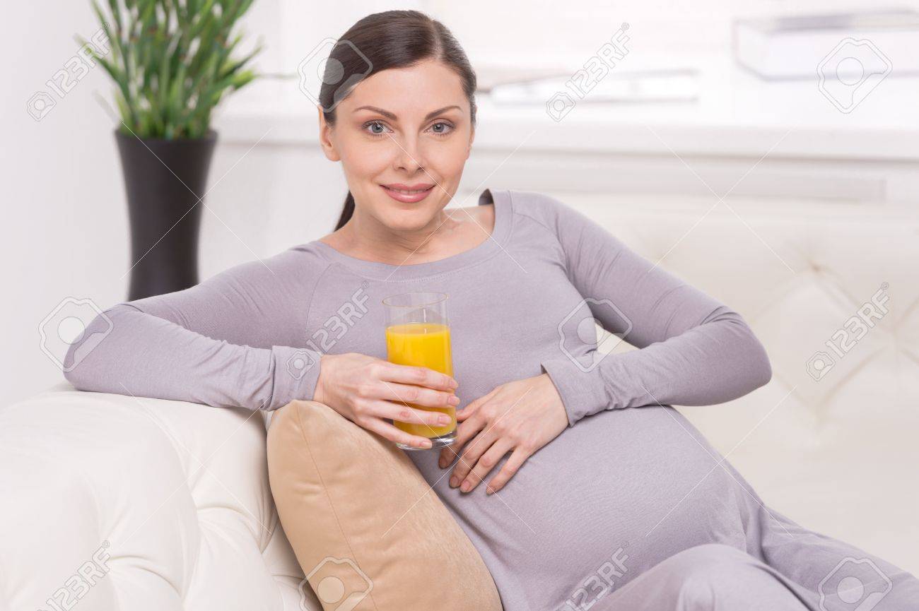 ジュース笑顔妊娠中の女性がソファに座って オレンジ ジュースのガラスを保持するいると妊娠中の女性 の写真素材 画像素材 Image