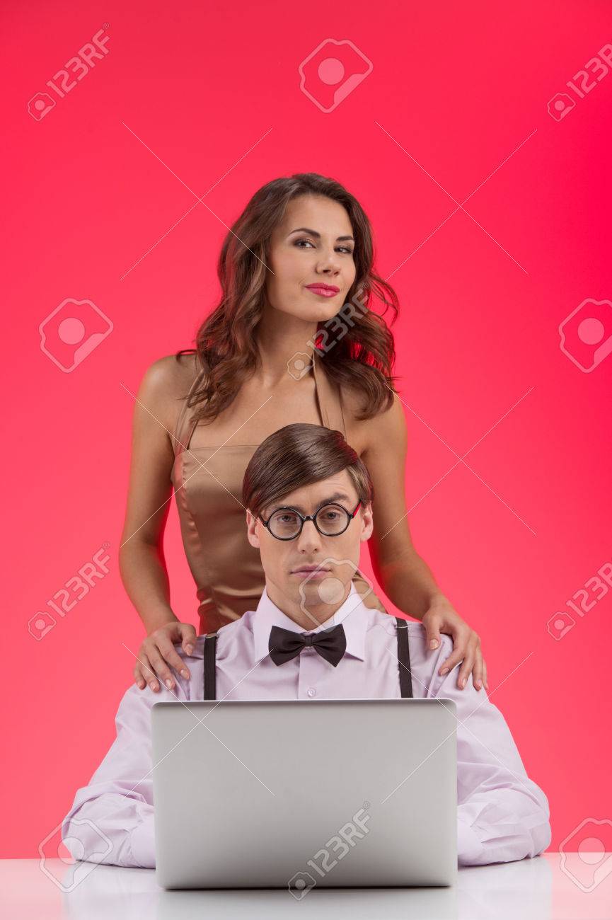 ガール フレンドとオタク 美しい若い女性は彼の背中の後ろに立っていると笑みを浮かべている間コンピューターで働いていた自信を持ってオタク男性 の写真素材 画像素材 Image