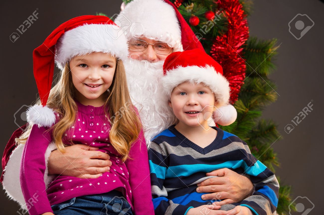 old kind santa claus holding two little kids on his knees smiling and looking at - Santa Claus With Kids old kind santa claus holding two little kids on his knees smiling and looking at - Santa Claus With Kids