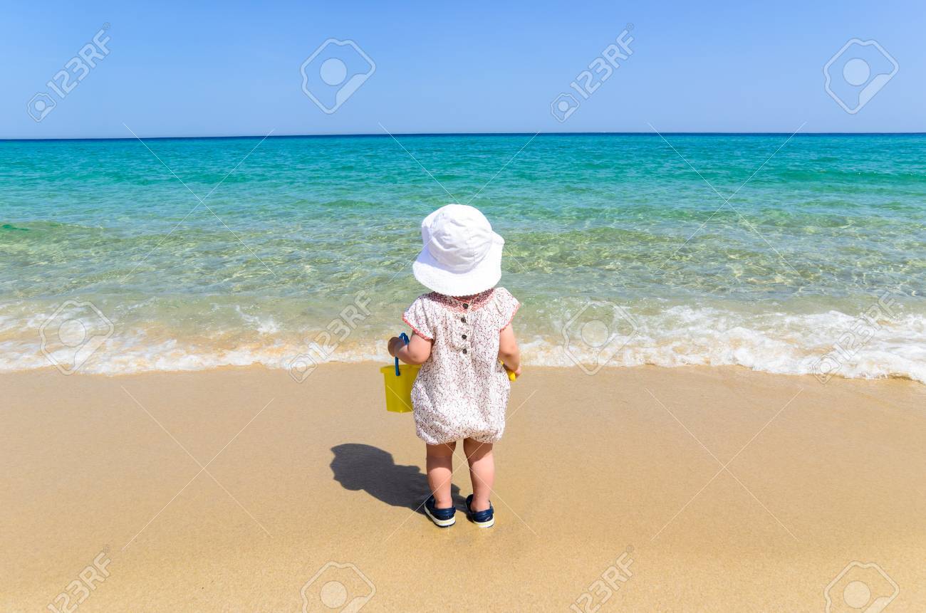 愛らしい少女の美しい水着と白い帽子子供バケツを押し 青緑色の海と青い空 コピー領域の背景上の休暇中にエキゾチックな白い砂浜のビーチで楽しんで の写真素材 画像素材 Image