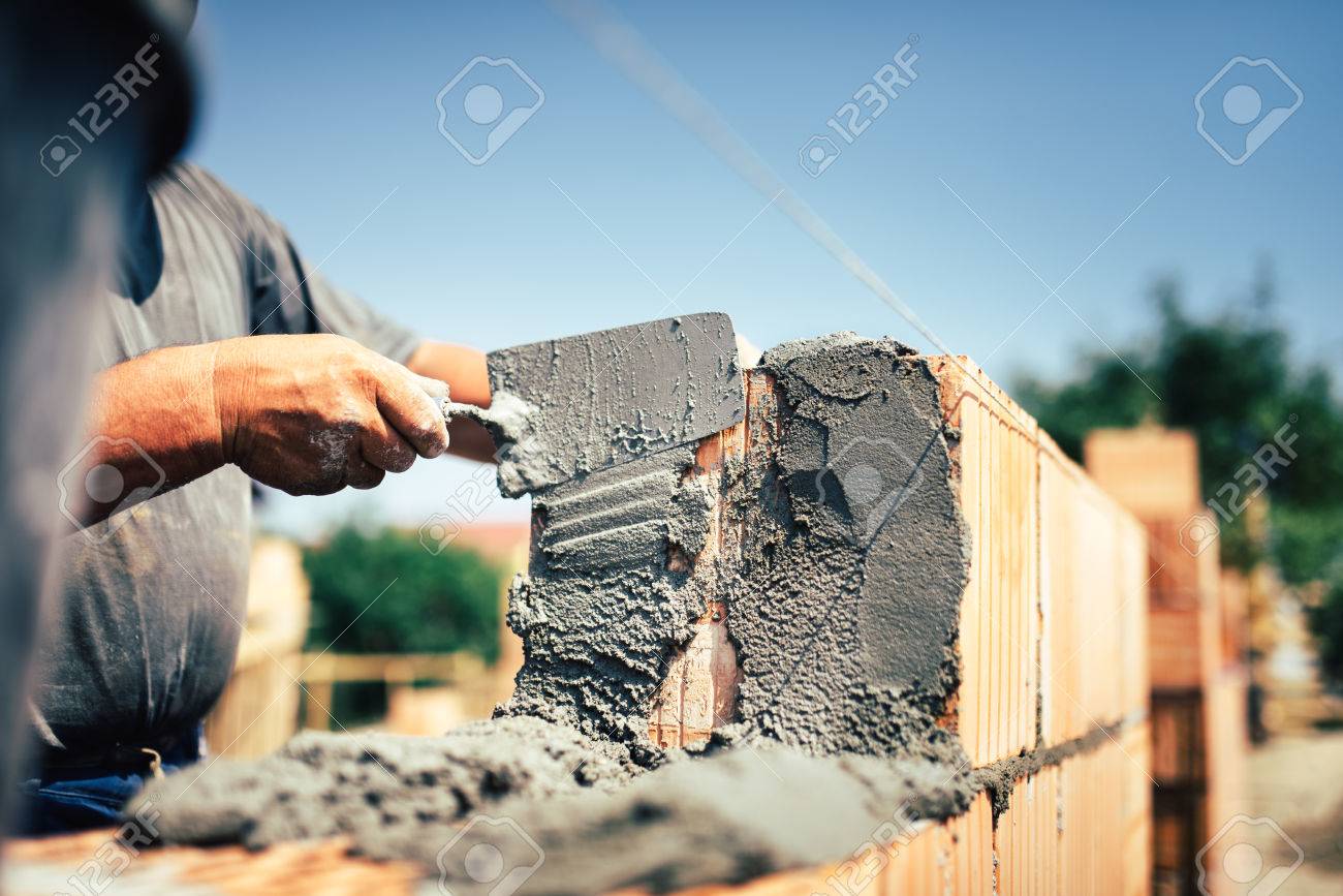 Bricklayer construction worker installing brick masonry on exterior wall with trowel putty knife - 71990920 Bricklayer construction worker installing brick masonry on exterior wall with trowel putty knife - 71990920
