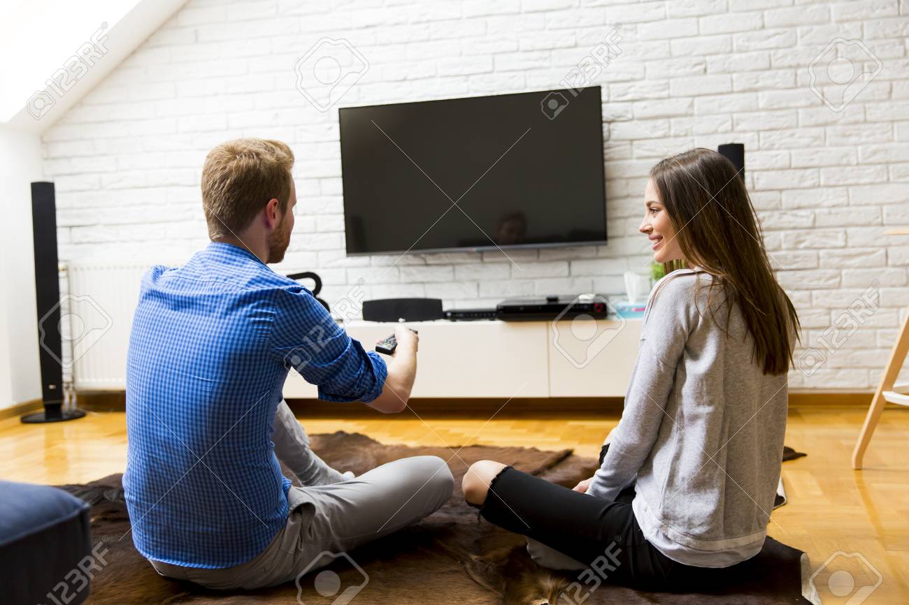 Young Couple Watching Television Sitting Comfortably On Floor