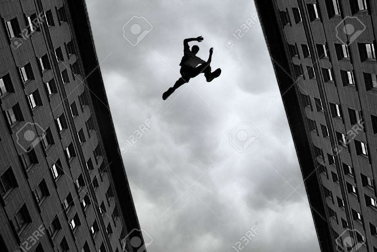 man jumping over building roof against gray sky background stock