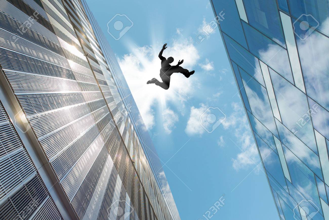 man jumping over building roof against blue sky background stock