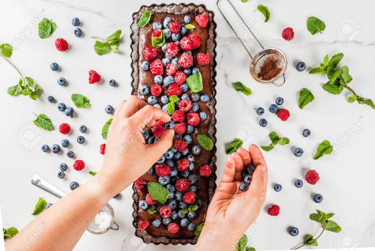 夏の自家製焼き菓子チョコレート クリームとチョコレート ケーキ タルト 女性はブルーベリー ラズベリー ミントの葉 粉砂糖とそれを飾る 白い大理石のテーブル 画像のコピー スペース平面図手します の写真素材 画像素材 Image