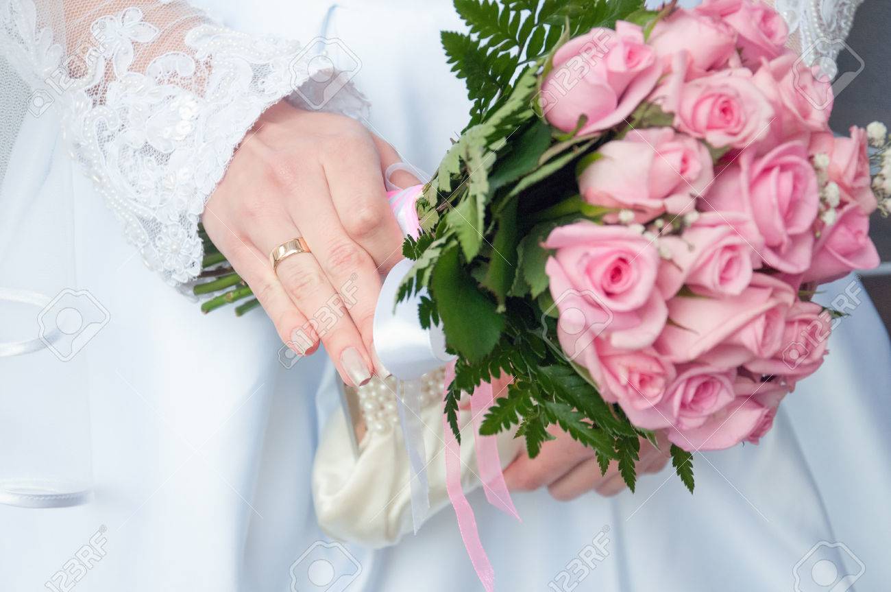 close up of bride hand holding wedding bouquet of roses stock photo